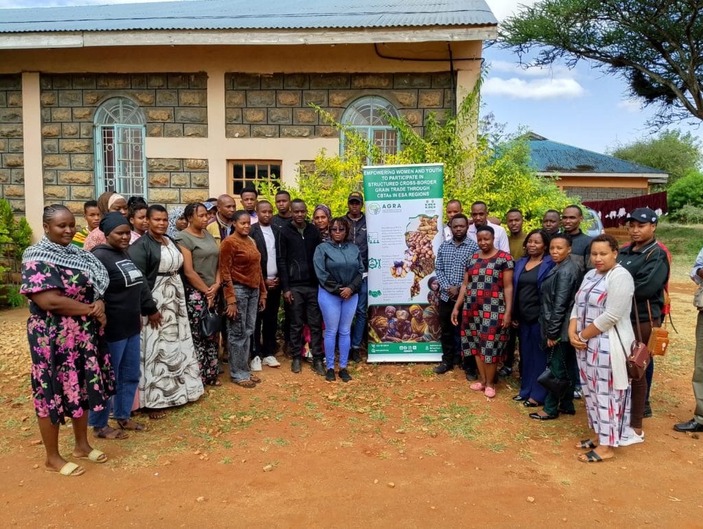 Group photo of Traders and Participants at Namanga cross-border training; diverse attire; banner highlights women, youth in trade; rural Kenya Tanzania setting with red soil