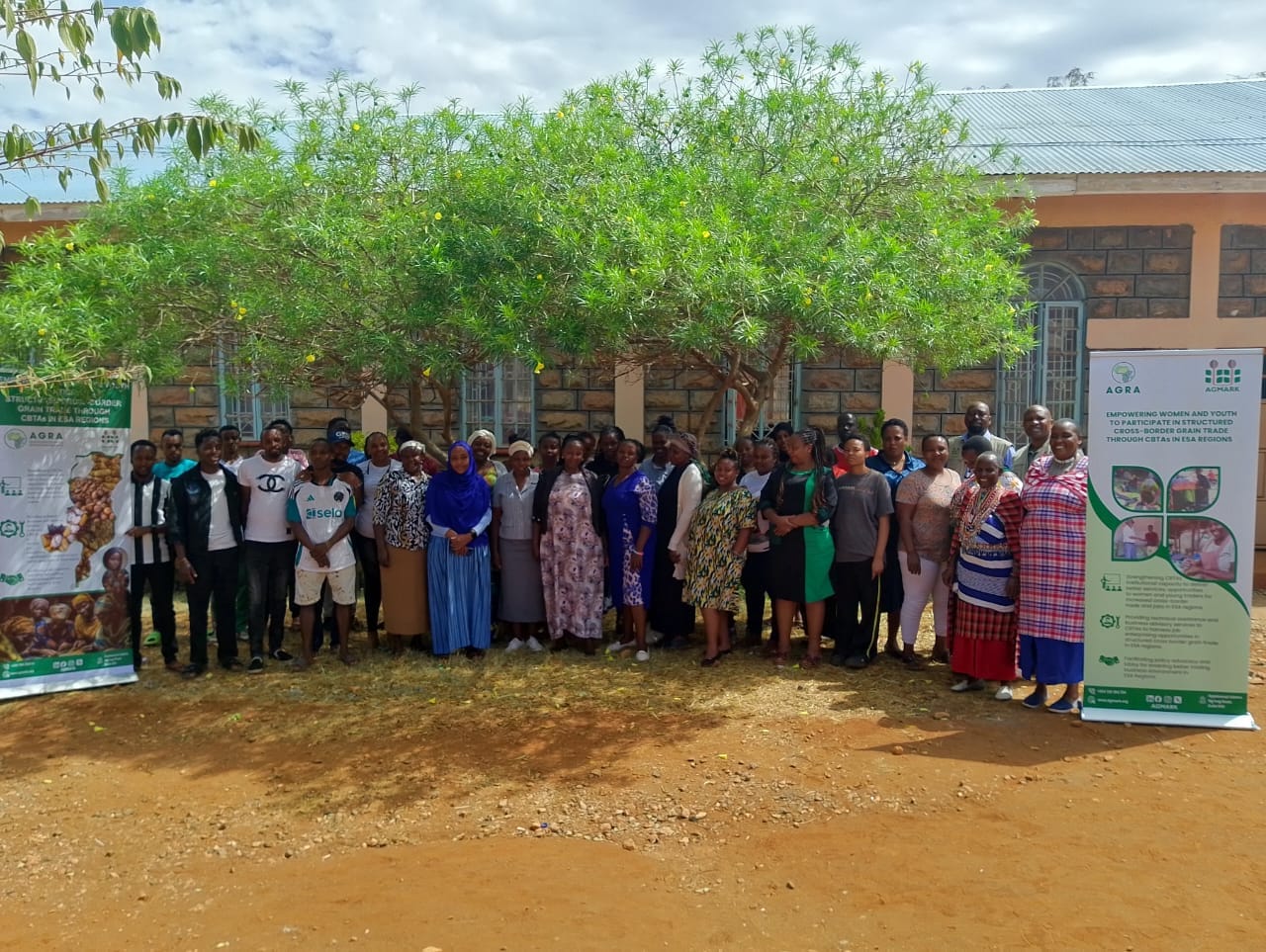 Documentary-style image of diverse group at stone building in Namanga, capturing cross-border grain trade empowerment event in rural setting
